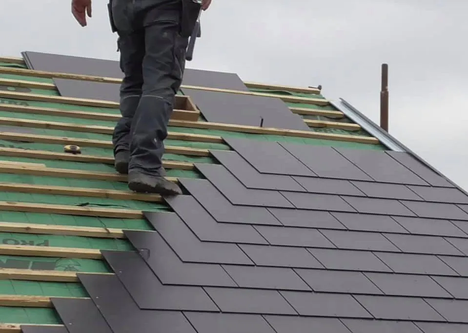 Roofer laying new slates over green breathable membrane and treated battens